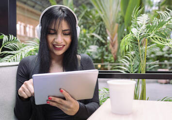 Junge schöne Frau trägt Kopfhörer, während sie ein digitales Tablet in einem Café benutzt - JCCMF01188