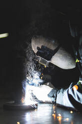 Male professional welder in welding helmet working at workshop - JAQF00252