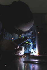 Männlicher Schweißer in Arbeitsschutzkleidung bei der Arbeit in einer Werkstatt - JAQF00254