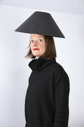 Mature woman with black lamp shade on head against white wall - PSTF00836