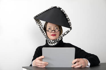 Frau mit schwarzem Lampenschirm hält digitales Tablet vor weißer Wand - PSTF00837
