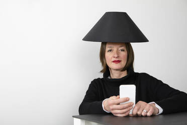 Ältere Frau mit schwarzem Lampenschirm, die ein Smartphone benutzt - PSTF00838