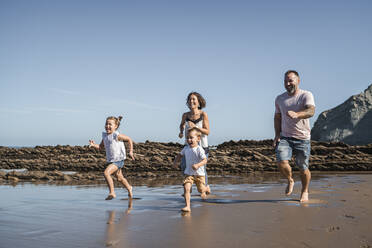 Cheerful family running at beach against sky - SNF01132