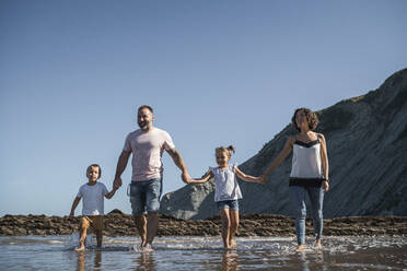 Family holding hands while walking at beach against sky - SNF01134