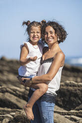 Smiling mother holding daughter while standing on flysch during sunny day - SNF01138