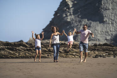 Girl watching parents swinging brother while walking at beach - SNF01141