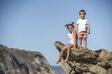 Spain, Gijon, group picture of three little girls sitting at rocky coast  stock photo