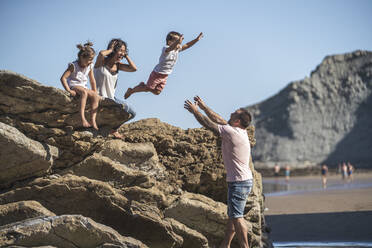 Carefree boy jumping onto father while mother and sister watching at beach - SNF01144