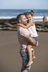 Lächelnde Tochter umarmt Vater am Strand an einem sonnigen Tag - SNF01146