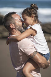 Lächelnder Vater, der seine Tochter am Strand trägt, an einem sonnigen Tag - SNF01147