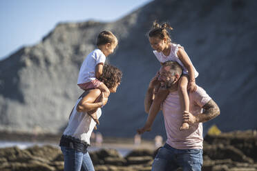 Cheerful parents carrying children on shoulder at beach - SNF01150