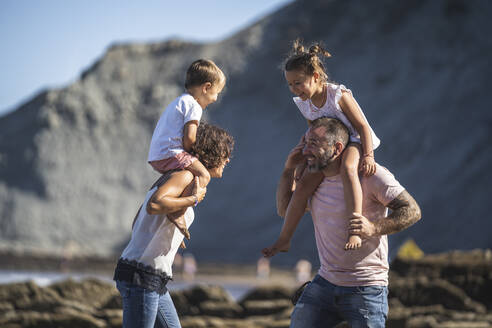 Fröhliche Eltern mit Kindern auf den Schultern am Strand - SNF01150