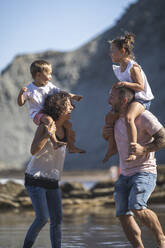 Cheerful parents with kids on shoulder enjoying at beach - SNF01151