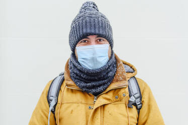 Mann in warmer Kleidung vor weißer Wand während einer Pandemie - PGF00412