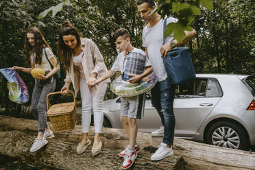 Eltern mit Kindern stehen beim Picknick auf einem Baumstamm im Wald - MASF21736