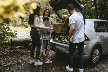 Family removing picnic things from car trunk in forest during vacation - MASF21738