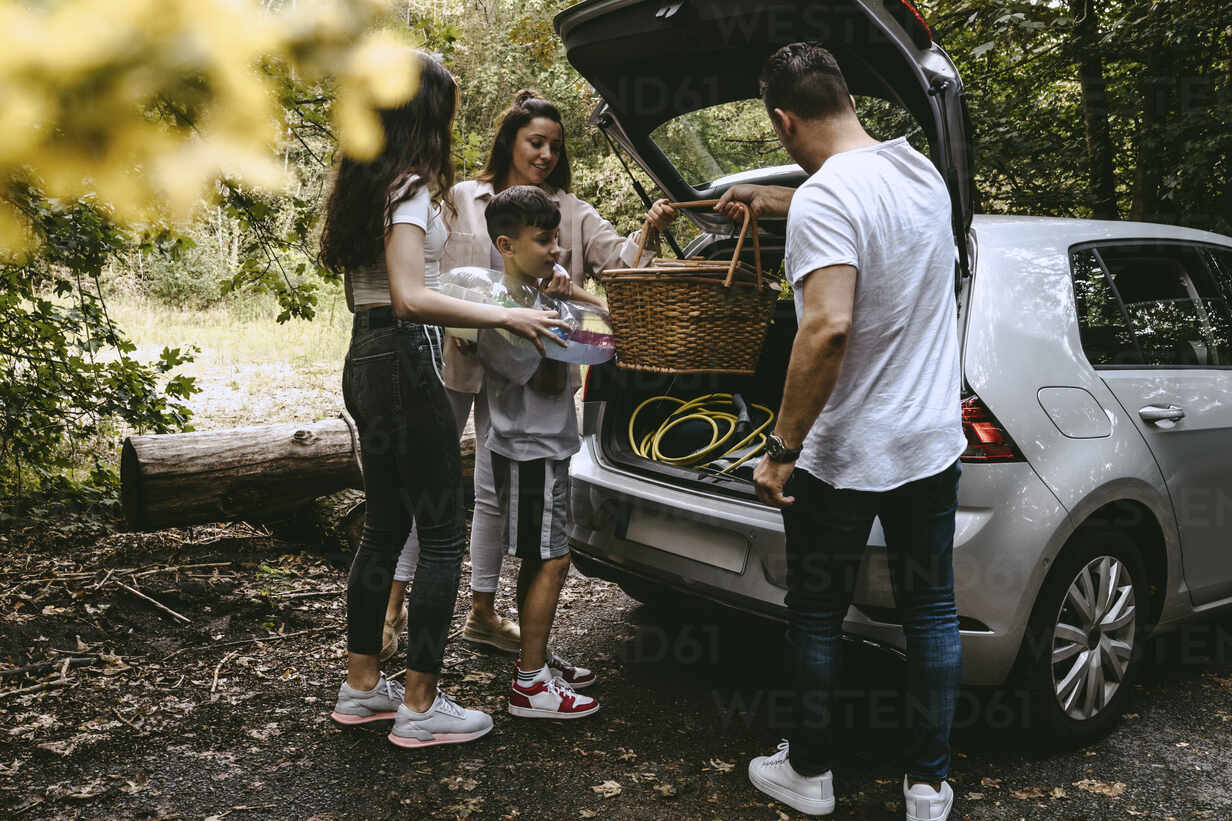 Familie beim Entfernen von Picknick-Sachen aus dem Kofferraum im Wald  während des Urlaubs, lizenzfreies Stockfoto