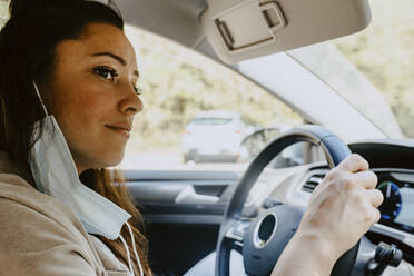 Woman sitting in electric car while looking away during COVID-19 - MASF21739