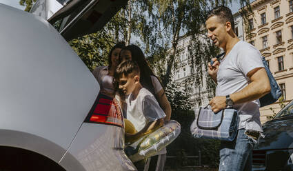 Family peeking in car trunk while standing on road during vacation - MASF21748