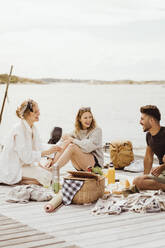 Glückliche junge Freunde verbringen ihre Freizeit auf einem Steg mit Blick auf Himmel und Meer - MASF21759