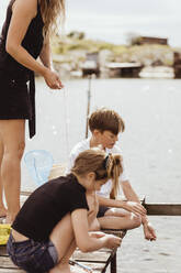 Midsection of mother standing while children fishing on sunny day - MASF21778