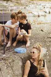 Mutter und Kinder mit Smartphone bei einem Picknick am Hafen - MASF21782