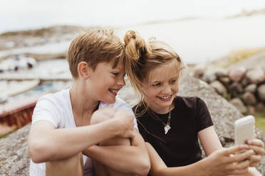 Lächelnder Bruder und lächelnde Schwester machen ein Selfie mit ihrem Smartphone im Yachthafen - MASF21786