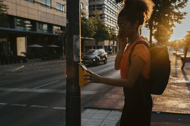 Side view of businesswoman pressing button on footpath while crossing street in city - MASF21818