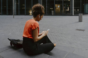 Geschäftsfrau, die ein Smartphone benutzt, während sie auf einer Treppe in der Stadt sitzt - MASF21822