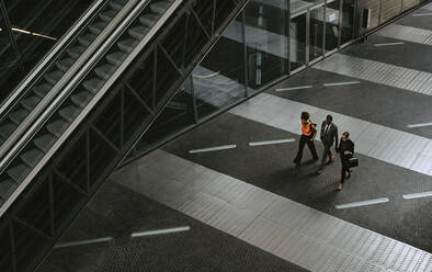 Männlicher Unternehmer mit weiblichen Kollegen, die sich beim Gehen auf der Rolltreppe unterhalten - MASF21832