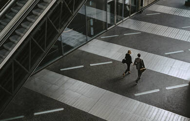 Rückansicht eines männlichen und eines weiblichen Kollegen, die eine Rolltreppe auf einem Gehweg benutzen - MASF21835