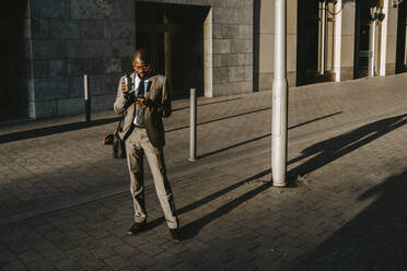 Geschäftsmann, der ein Smartphone benutzt, während er auf einem Fußweg in der Stadt steht - MASF21842