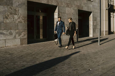 Female and male colleagues discussing while walking on footpath in city - MASF21843