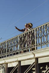 Älterer Mann zeigt auf eine Frau auf einer Brücke vor blauem Himmel - MASF21865