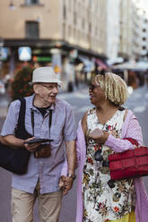 Happy senior couple holding hands walking in city - MASF21877
