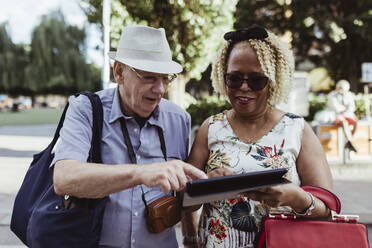 Lächelndes älteres Paar, das an einem sonnigen Tag auf der Straße ein digitales Tablet benutzt - MASF21883