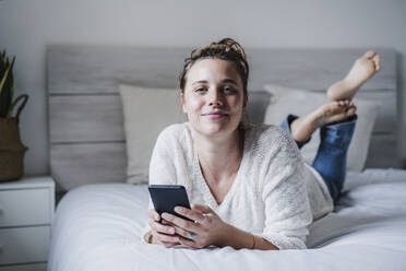 Woman using smart phone while lying on bed at home - EBBF02418