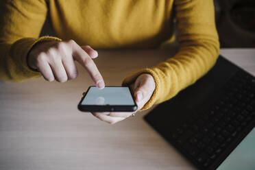 Frau, die ein Smartphone benutzt, während sie mit einem digitalen Tablet im Home Office sitzt - EBBF02427