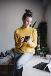 Young woman using mobile phone while sitting by digital tablet on table at home - EBBF02451