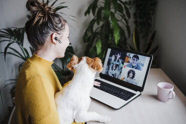 Frau spricht mit Freunden per Videokonferenz über ein digitales Tablet, während sie mit ihrem Haustier zu Hause sitzt - EBBF02452