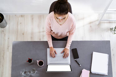 Junge Frau arbeitet am Laptop, während sie zu Hause im Büro sitzt - GIOF11047