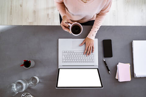 Young woman having coffee while using laptop while sitting at home stock photo