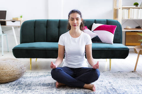 Junge Frau meditiert zu Hause sitzend, lizenzfreies Stockfoto