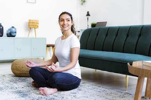 Junge Frau lächelnd beim Yoga zu Hause sitzend - GIOF11053