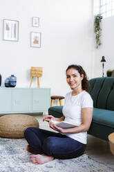 Smiling woman reading book while sitting at home - GIOF11055