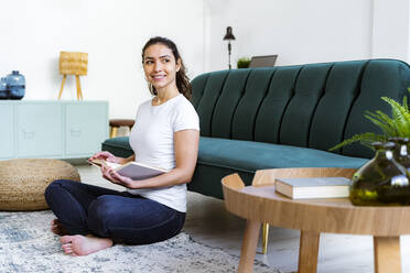 Smiling woman with book looking away while sitting at home - GIOF11056