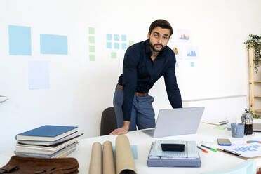 Young businessman leaning at desk in office - GIOF11067