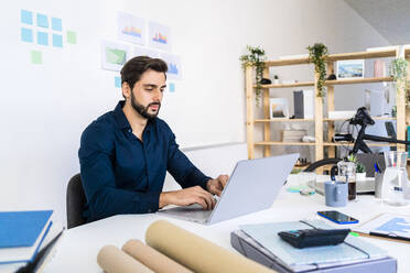 Young businessman working on laptop in office - GIOF11069