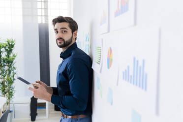 Männlicher Unternehmer mit digitalem Tablet, der in einem Büro an der Wand steht - GIOF11088