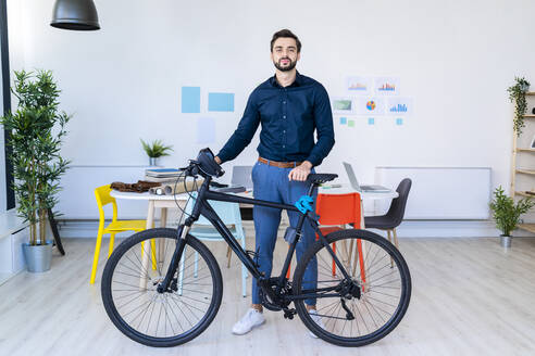 Männlicher Unternehmer mit Fahrrad im Büro stehend - GIOF11092